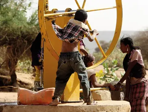 Enfants nigériens pompant l'eau d'un puits villageois équipé d'une roue à godets jaune